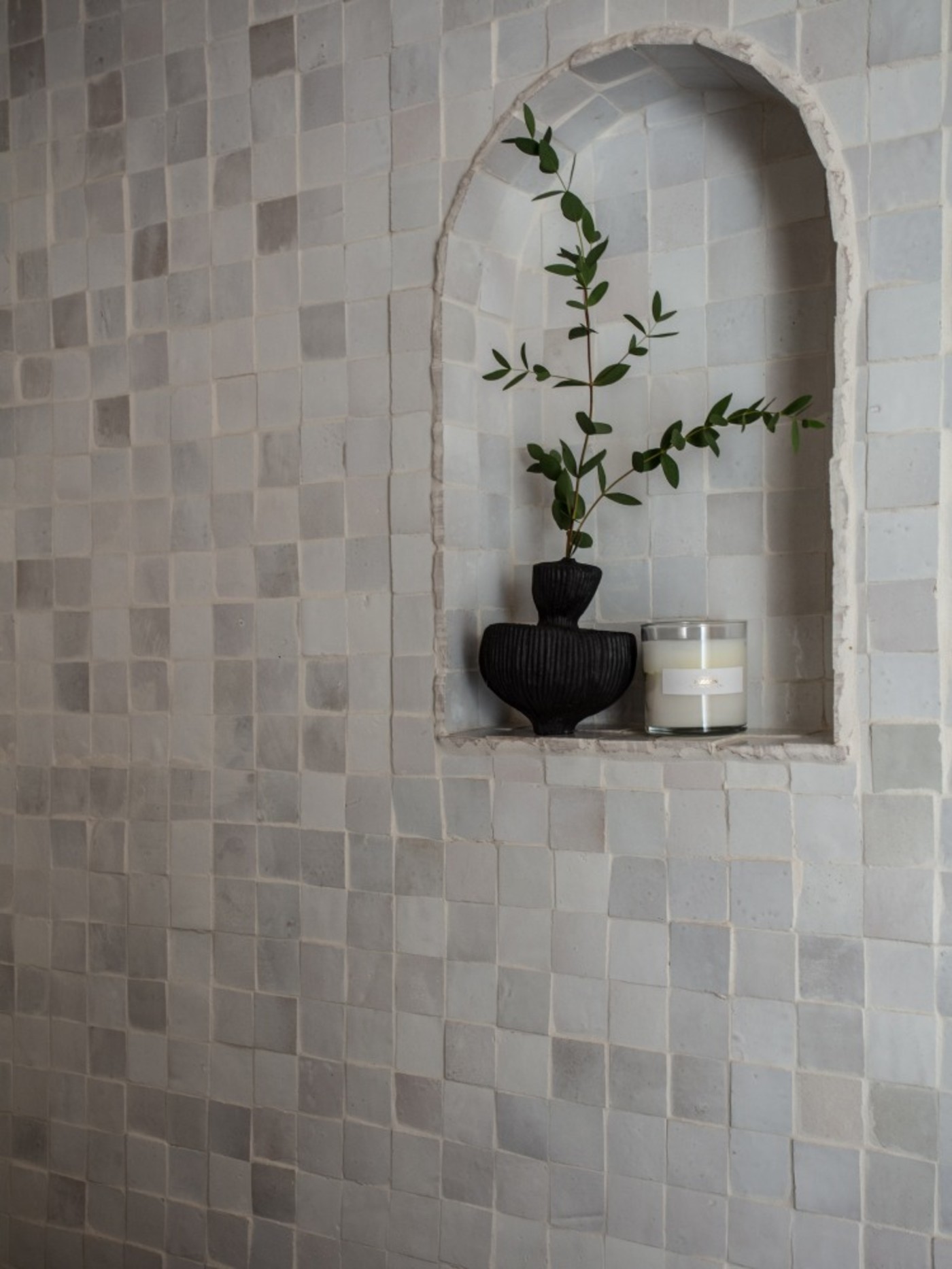 a bathroom with a white tiled wall and wall niche with a potted plant.