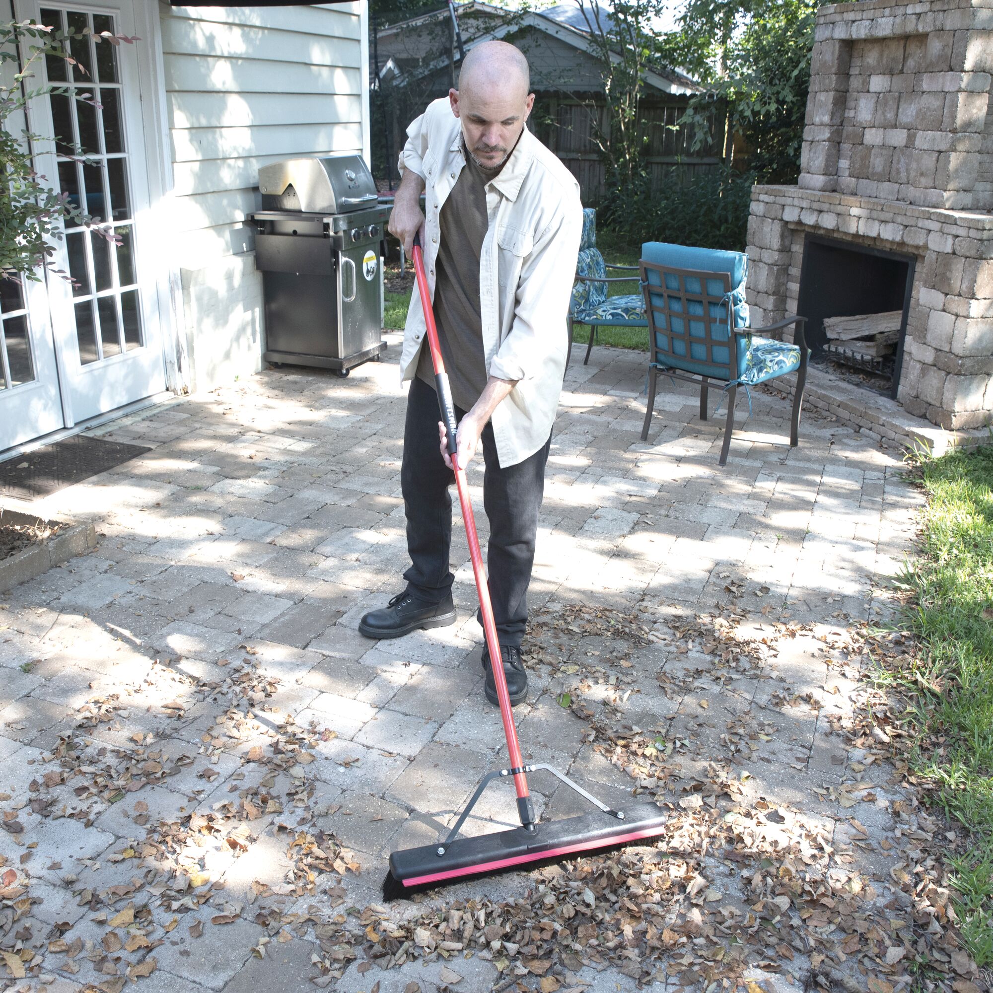 24 inch push broom with built in squeegee being used by a person to push leaves from the stone pavement.