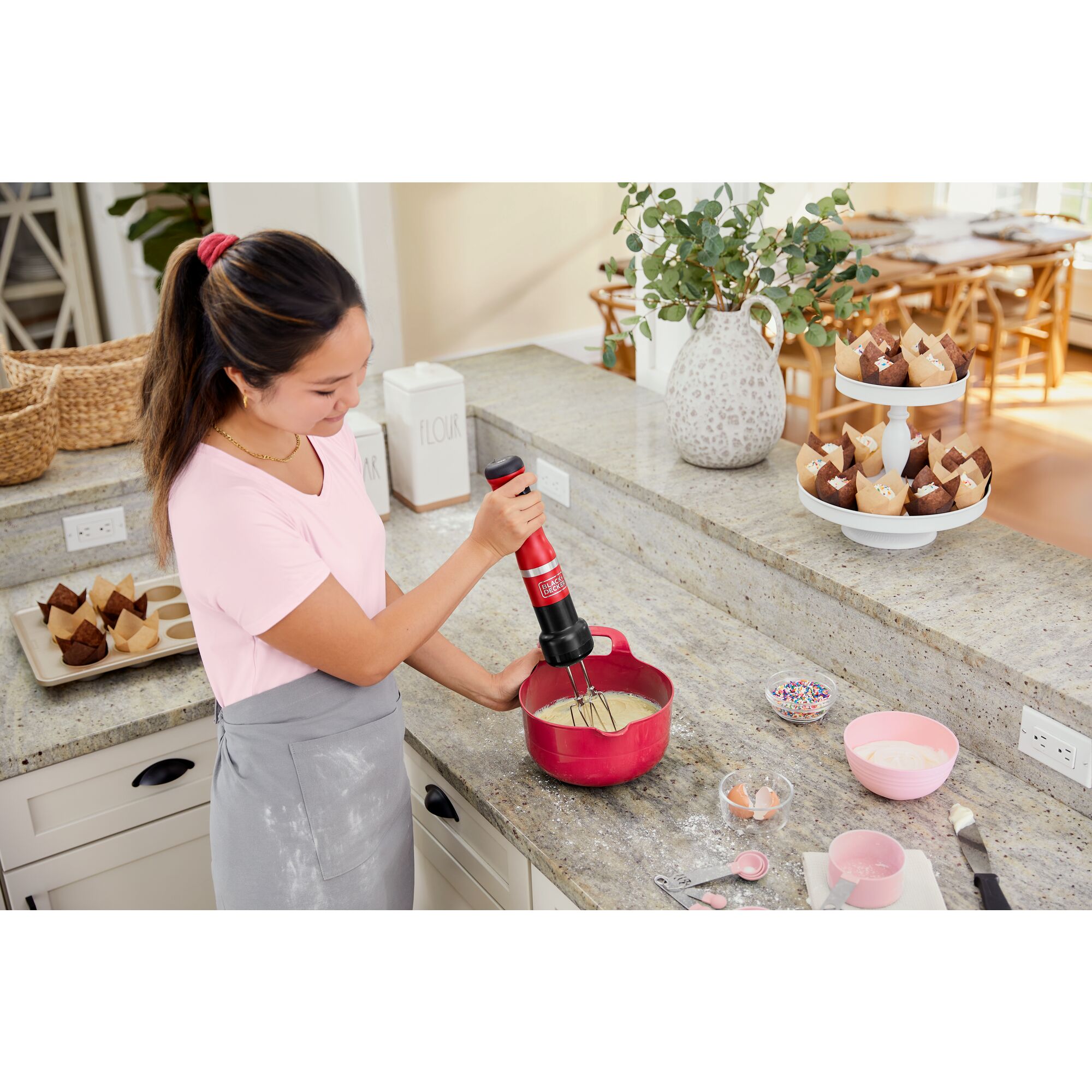 Model using the red, BLACK+DECKER kitchen wand hand mixer attachment to mix cupcake batter