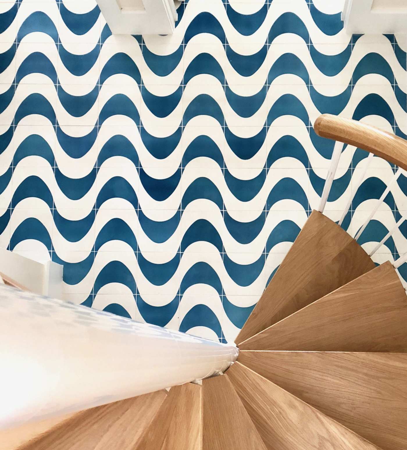 a spiral staircase leading to a tile floor with a blue and white wavy pattern.