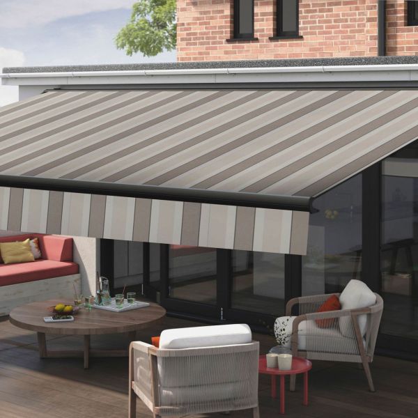 Striped beige-and-gray retractable awning, extended from the wall above sliding glass doors with a vertically striped valance; shading a sunlit brick-walled patio with lounge chairs and a low coffee table.