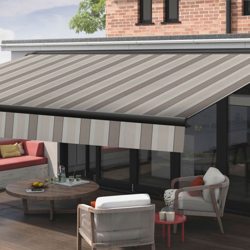 Striped beige-and-gray retractable awning, extended from the wall above sliding glass doors with a vertically striped valance; shading a sunlit brick-walled patio with lounge chairs and a low coffee table.