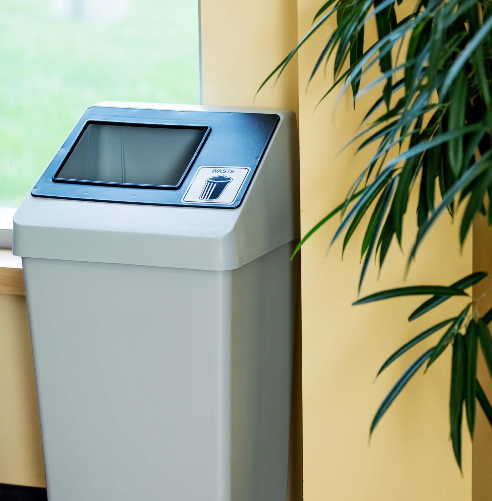 durable injection molded plastic waste bin with sloped lid and restrictive black opening in a college cafeteria