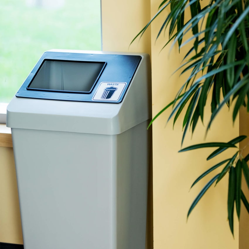durable injection molded plastic waste bin with sloped lid and restrictive black opening in a college cafeteria
