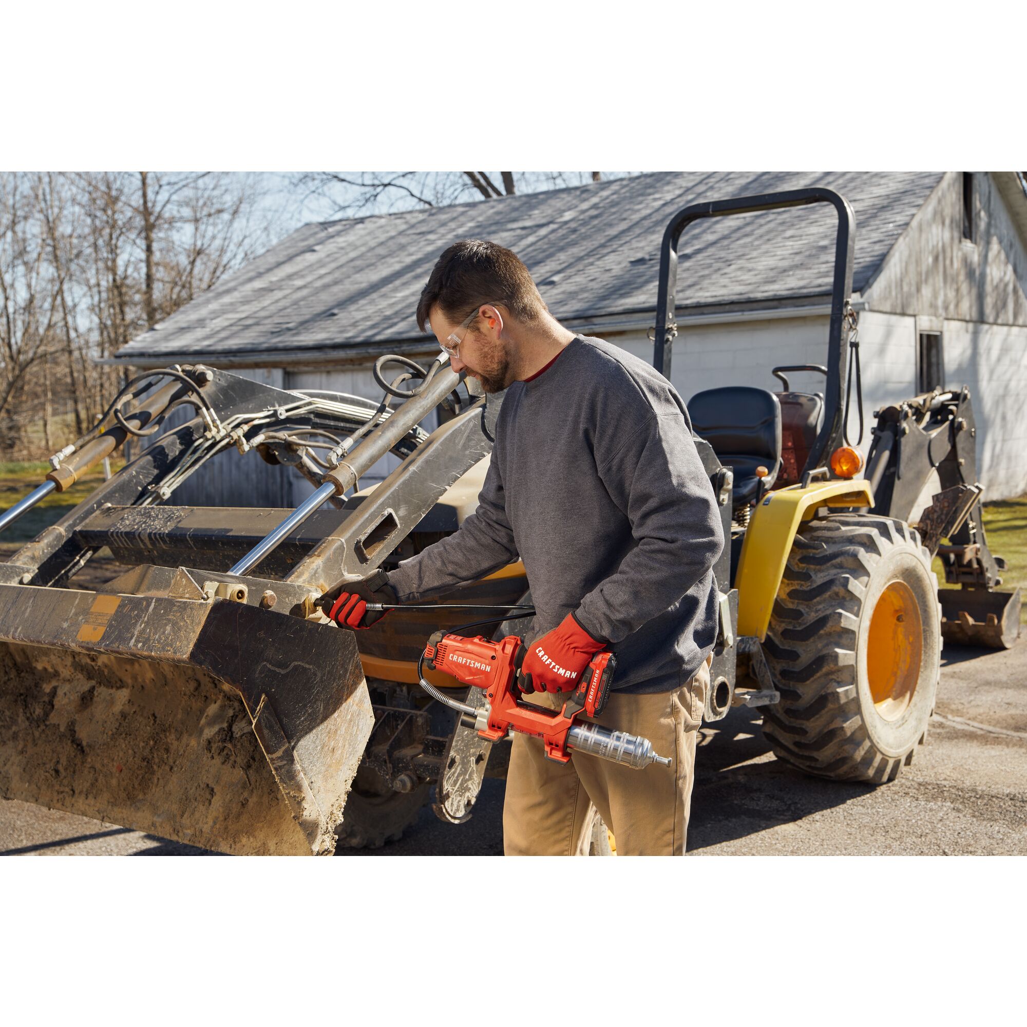Photo of end-user applying grease with grease gun to farm equipment.