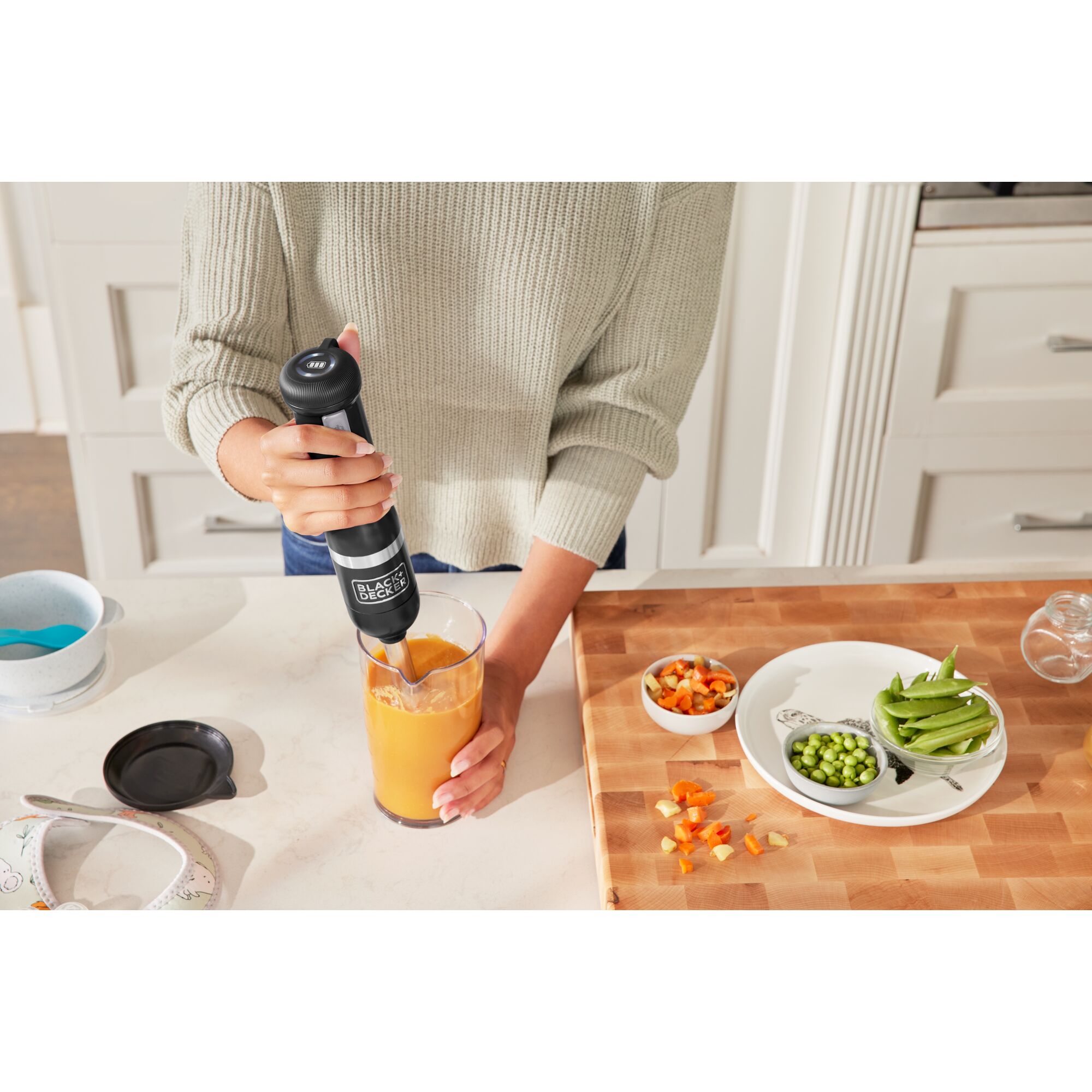 Talent using the black, BLACK+DECKER kitchen wand immersion blender to prepare baby food