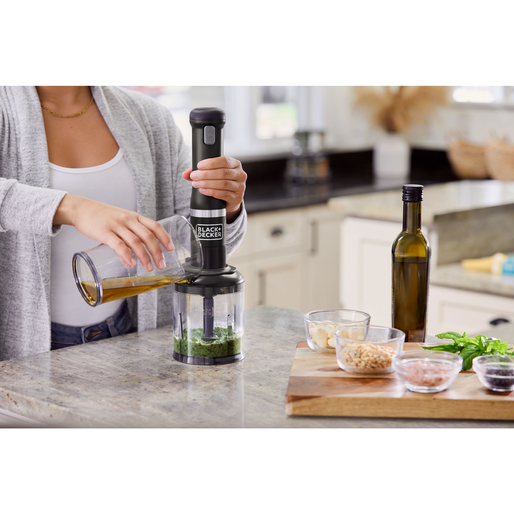 Model pouring olive oil in through the port of the BLACK+DECKER kitchen wand food chopper attachment