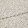 Textured beige-and-white fabric with an abstract, twiglike pattern, folded and layered once; close-up on a flat surface with soft, even lighting, suggesting a fabric sample or upholstery swatch.