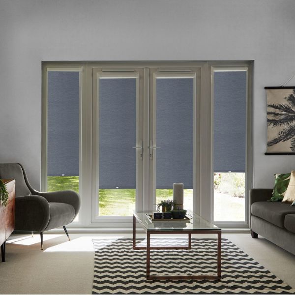 Gray roller blinds cover French doors and sidelights, textured panels with two bottoms slightly raised to show lawn. They are lowered, filtering daylight. Living room with armchair, sofa, coffee table.