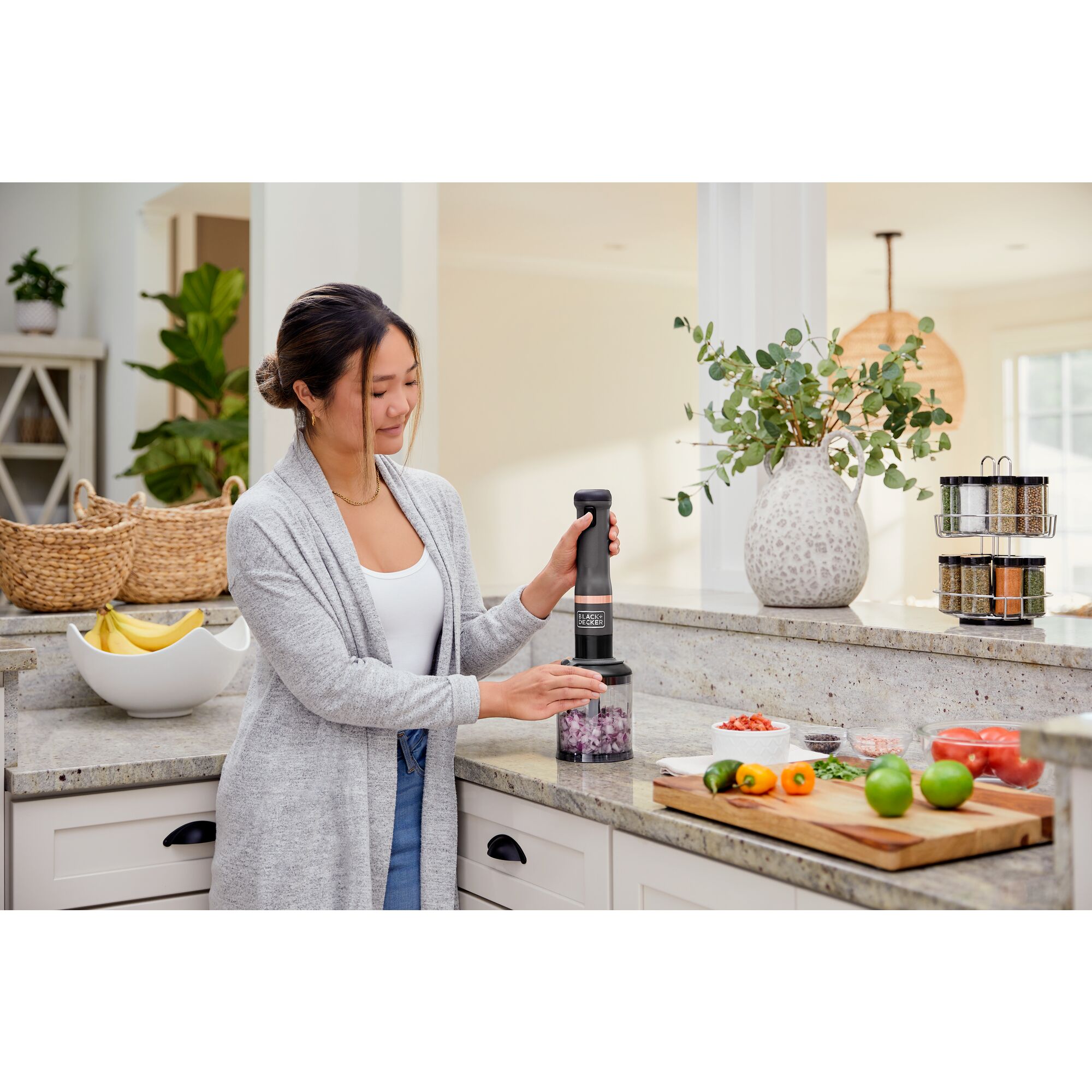Model using the grey, BLACK+DECKER kitchen wand food chopper attachment to chop onions