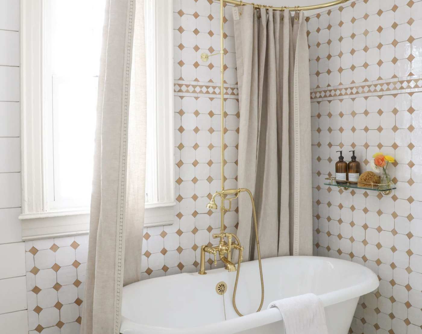 a bathroom with white and gold tiled wall and a claw foot tub.