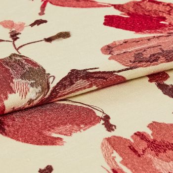 Cream jacquard fabric with large red floral motifs, folded once so layers overlap; embroidered sheen and textured stitching visible in a close-up, studio-lit product shot.