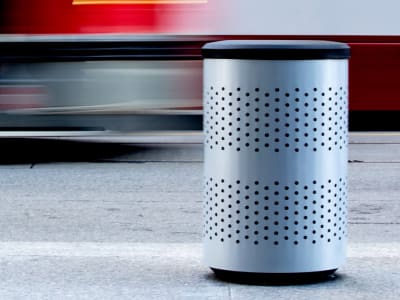 silver powder coated steel recycling bin with blue plastic lid sitting at a busy downtown patio area