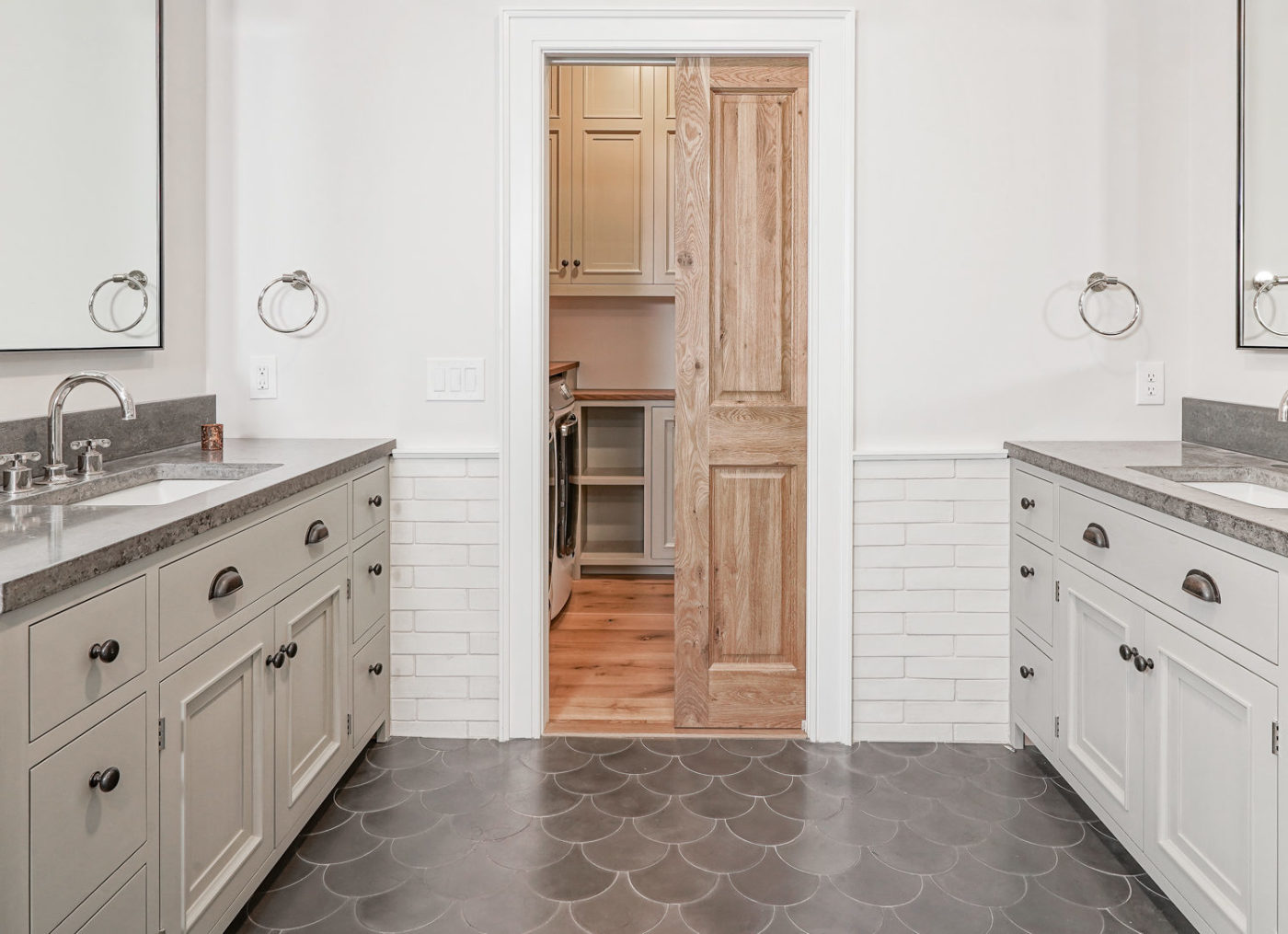 a bathroom with a grey tile floor, two sinks, and a door.