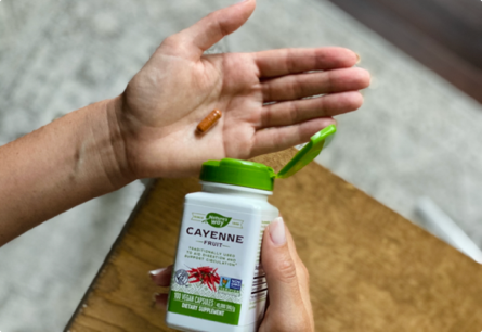 A hand pouring a Cayenne Fruit capsule into their other hand.