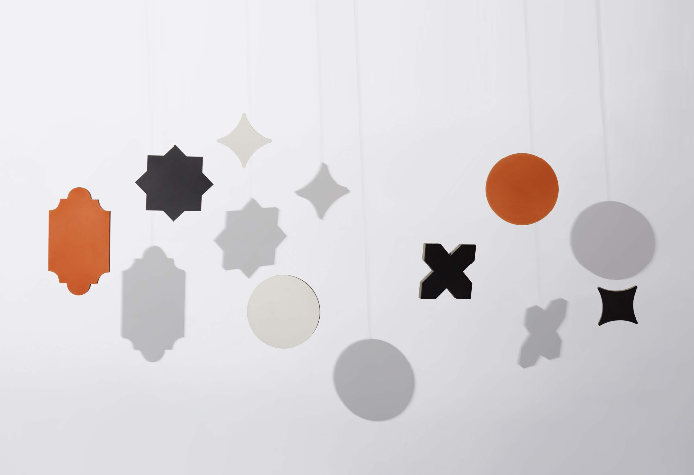 a group of different multicolored shapes and their shadows hanging from strings on a white wall.