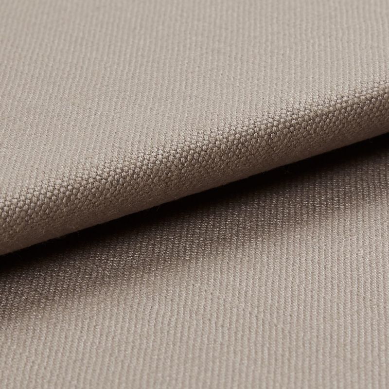Beige tightly woven upholstery fabric, folded with an overlapping edge across the frame, revealing a pebble-like weave; close-up macro view with soft neutral lighting and plain background.
