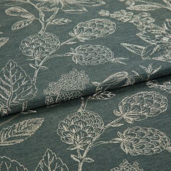 Dark teal fabric with white stitched botanical motifs (artichoke-like blooms and leaves), folded across the center, displaying layered, textured weave under soft, neutral studio lighting.