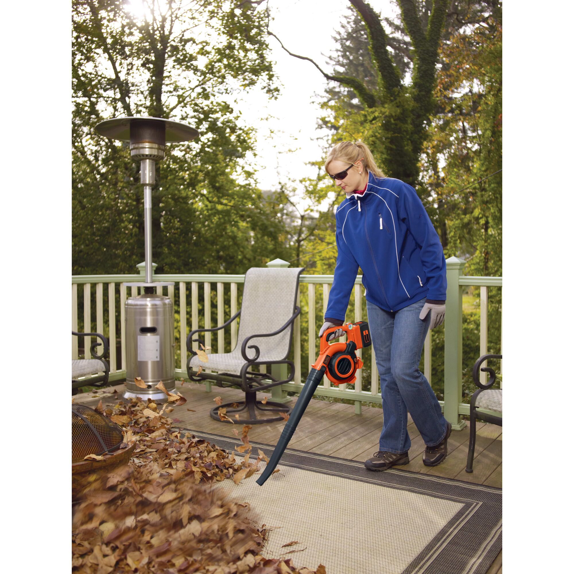 Woman using Cordless Leaf Blower/Vacuum to clear leaves from a deck with outdoor furniture.