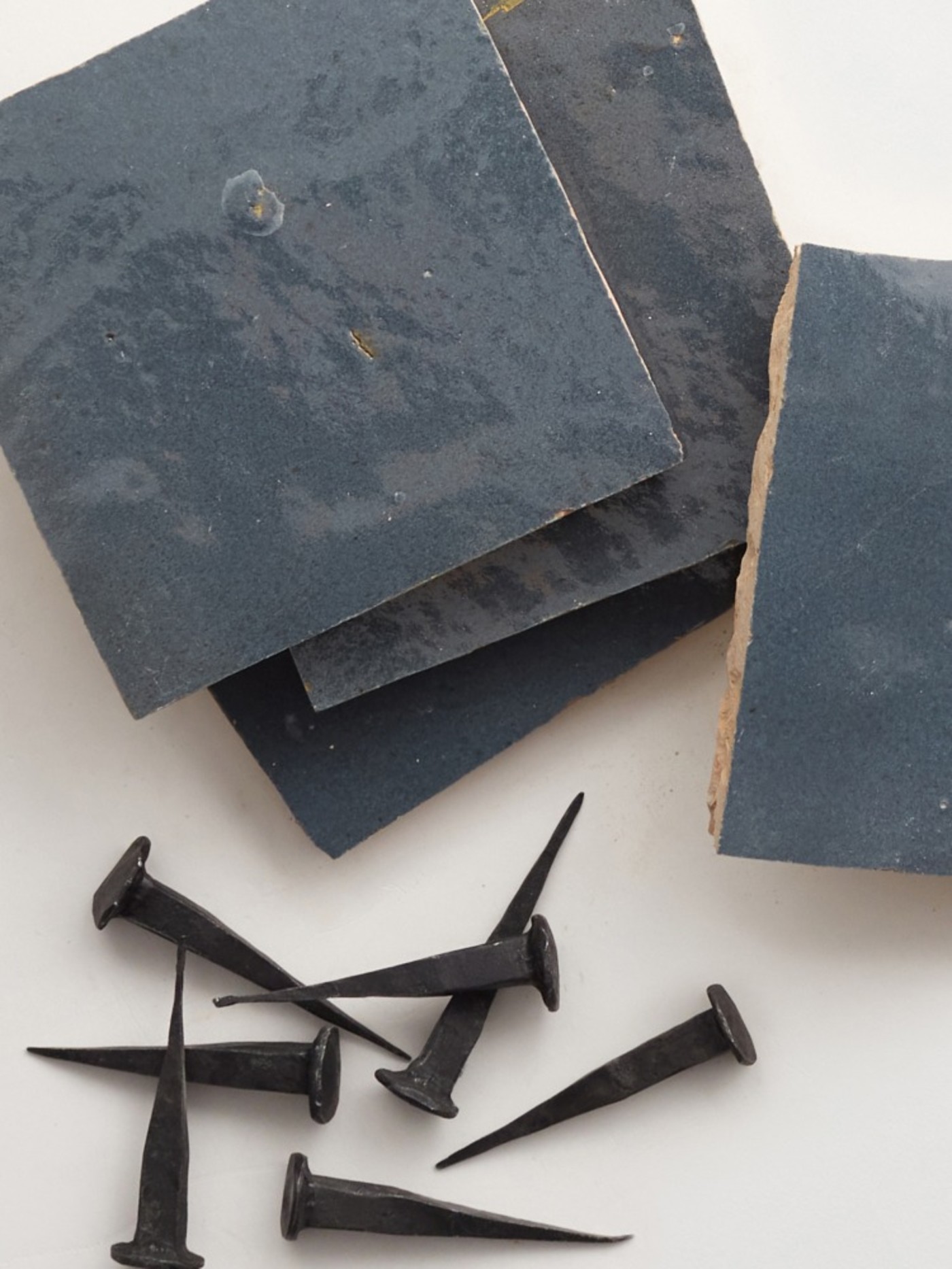 a pile of blue tiles and nails on a white surface.