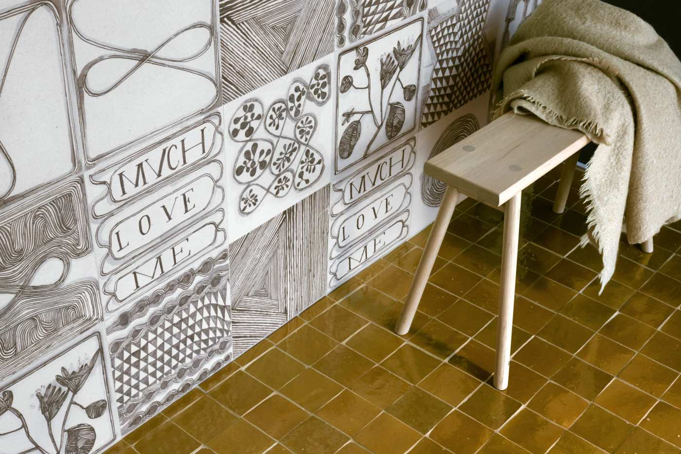 a wooden stool with a blanket on it in front of a tiled wall.