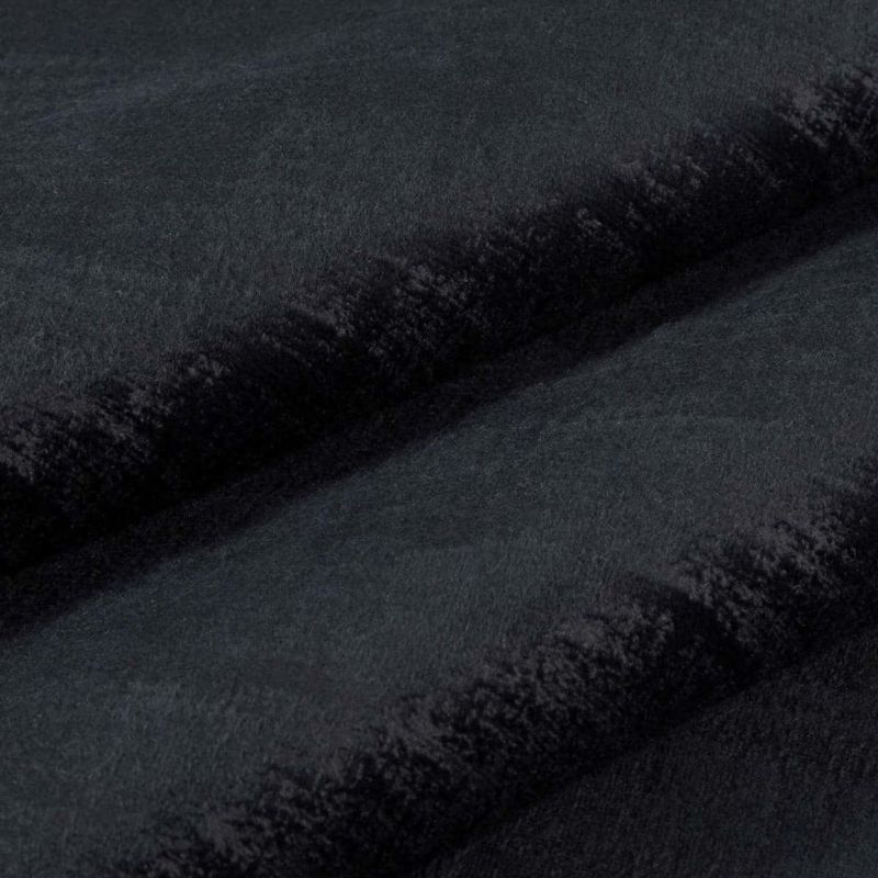 Black plush faux-fur fabric folded into two horizontal ridges, dense short pile and velvety nap; folds cast soft shadows in a close-up, evenly lit studio view.