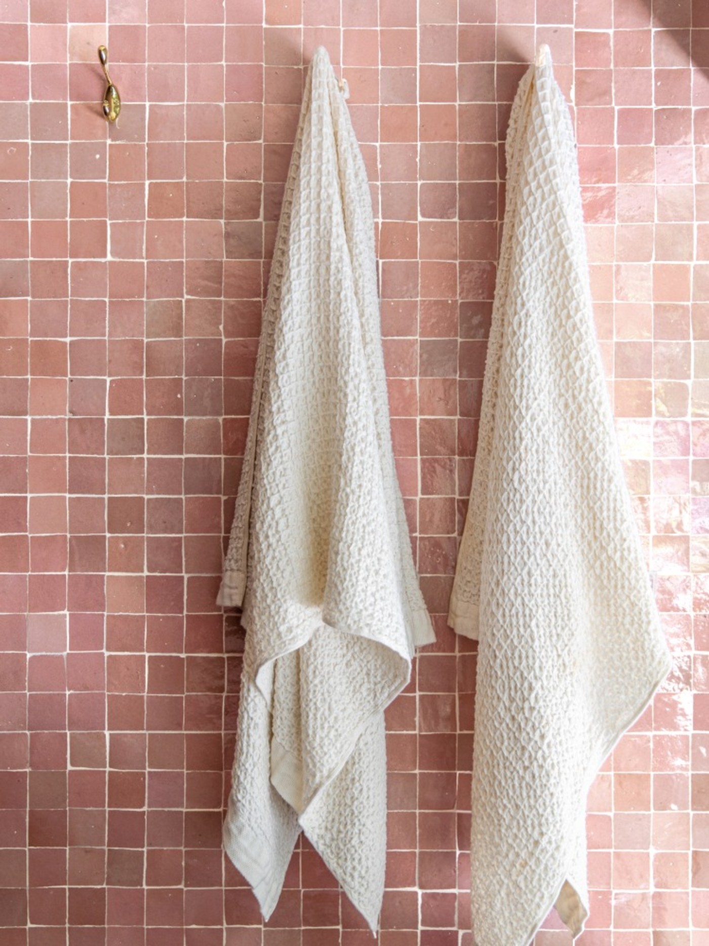 two towels hanging on a pink tiled wall.