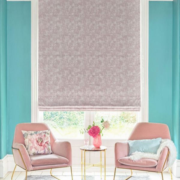 Roman blind, lowered over the window with a textured mauve pattern, filtering daylight; bright sitting room with teal walls, two pink armchairs, a gold side table and fresh flowers.