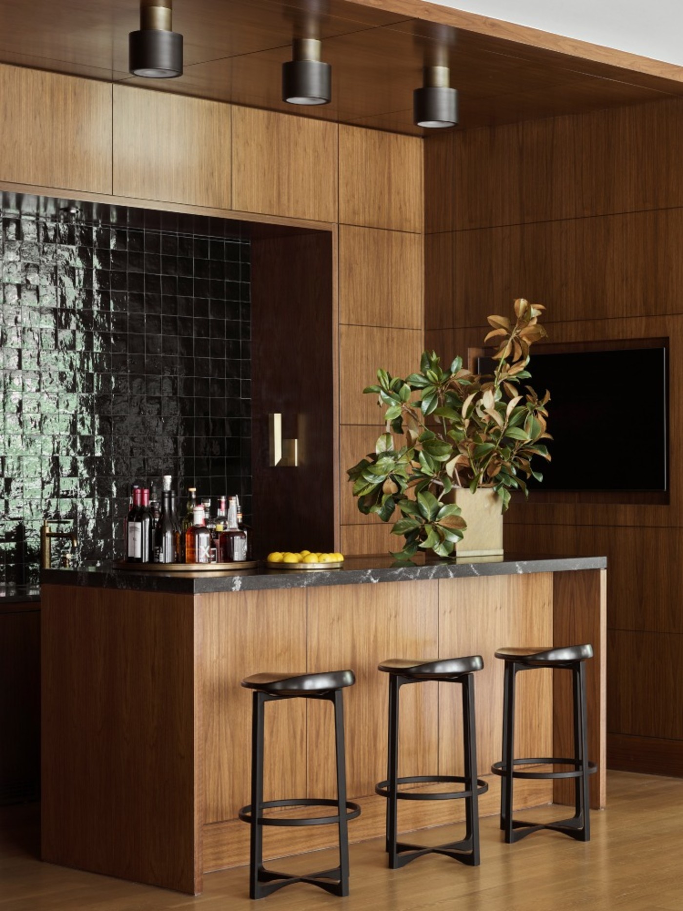 a wooden bar with stools and black tile wall.