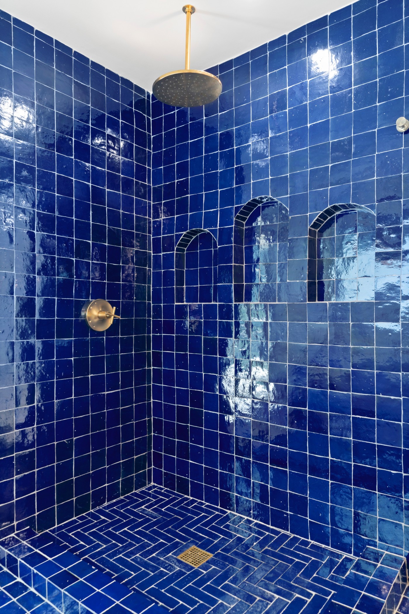 a blue tiled shower with a gold shower head.