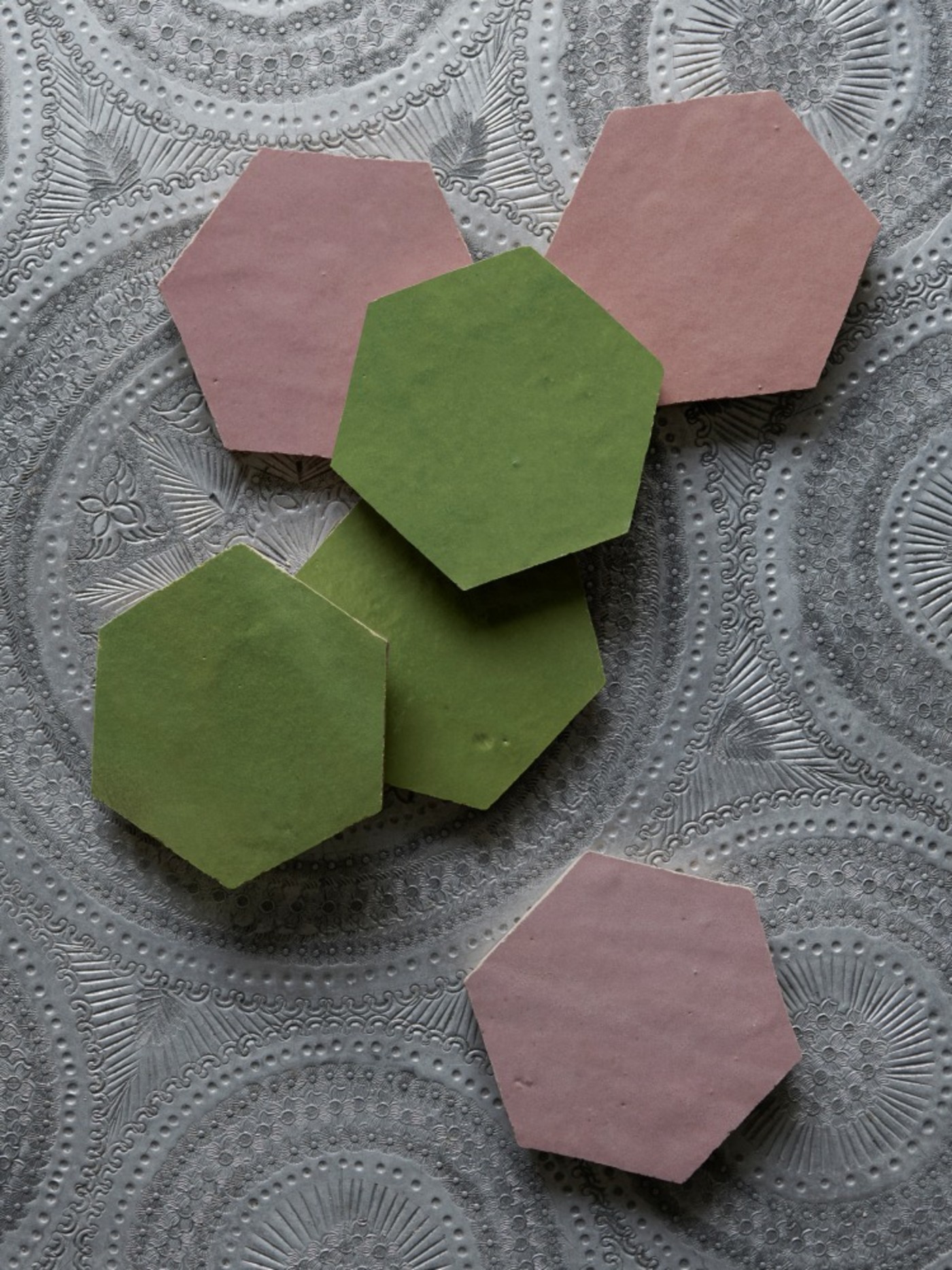 a set of pink and green hexagonal tiles on a silver patterned table.