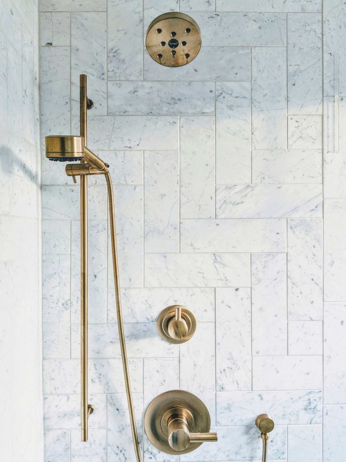 a white marble tiled shower with a brass shower head and faucet.