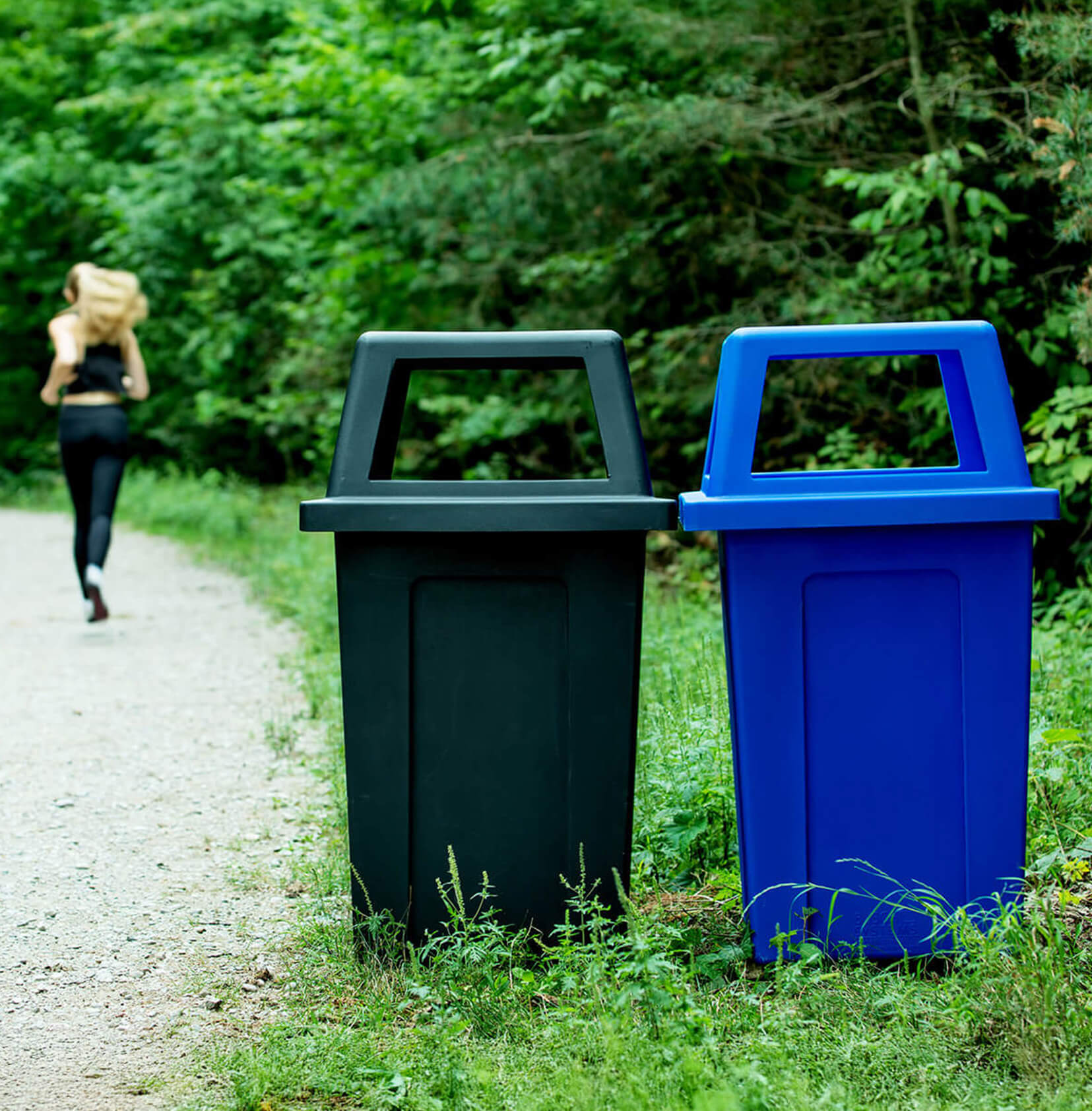 durable outdoor black waste container and blue recycling container with canopy lids sitting on a walking trail in the forest