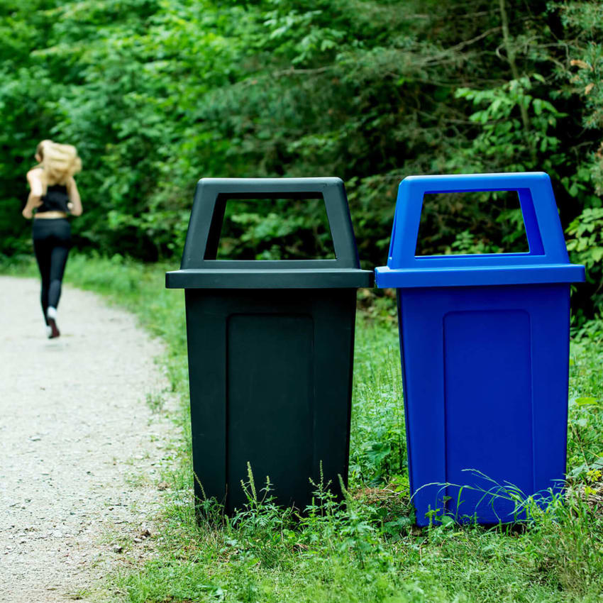 durable outdoor black waste container and blue recycling container with canopy lids sitting on a walking trail in the forest