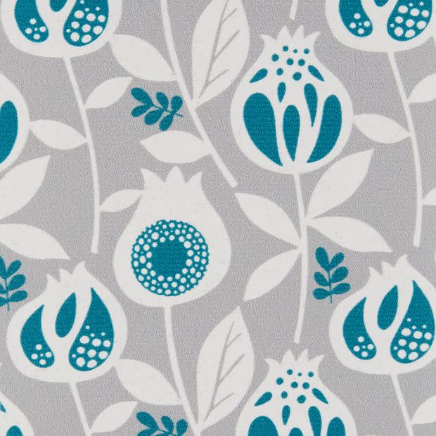 Wallpaper featuring repeating stylized pomegranate motifs in teal and white on a textured light-gray background; the printed fabric covers a flat surface, shown with even diffuse lighting.
