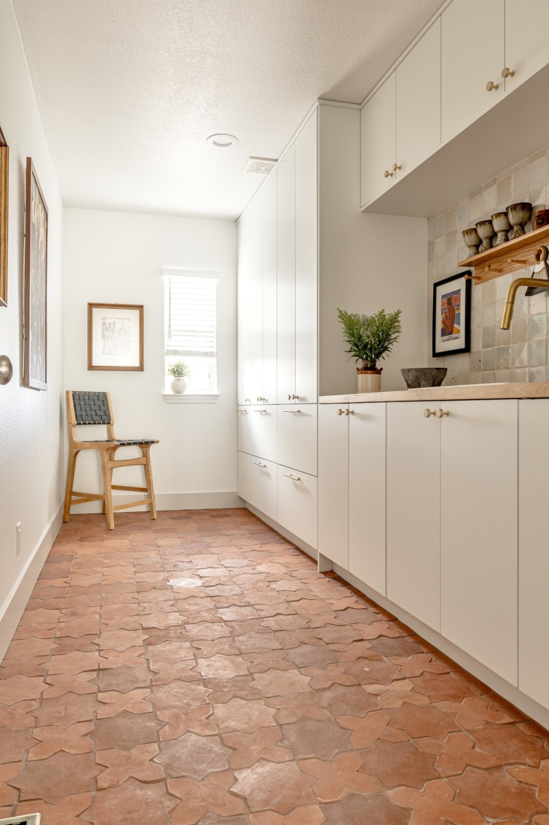 a kitchen with white cabinets and a red tile floor.