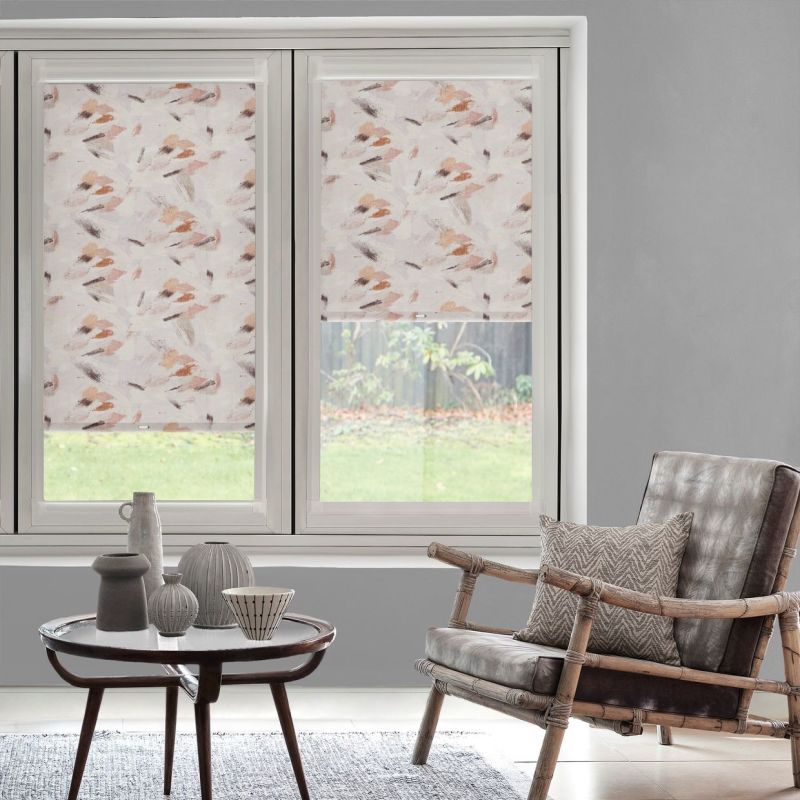 Patterned roller blinds with soft pink-beige brushstroke design cover two adjacent windows—left fully lowered, right halfway—filtering daylight and partially revealing grassy backyard; living room with chair and coffee table.