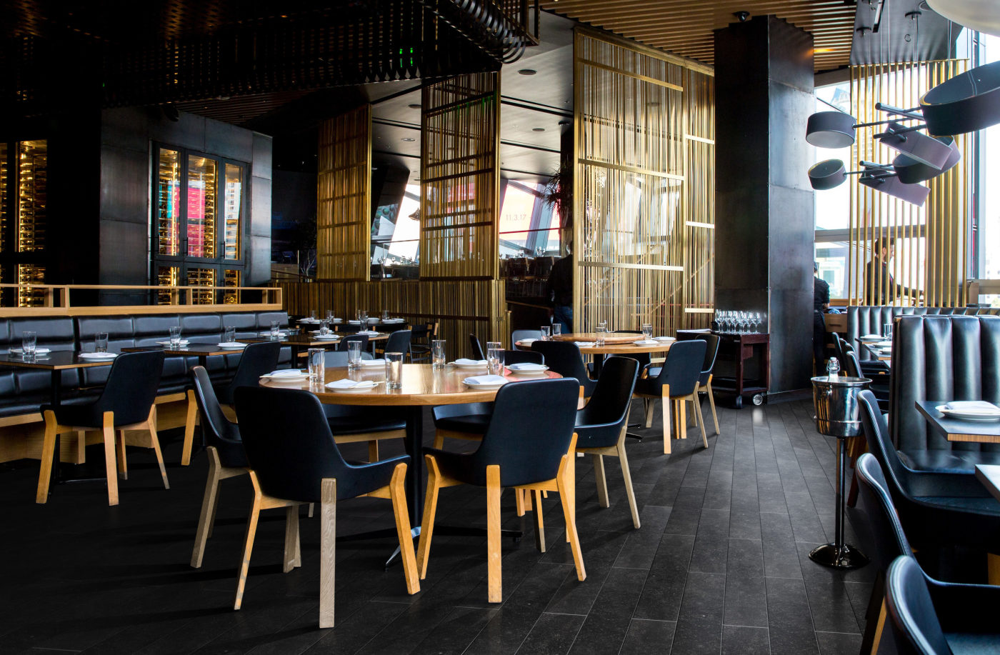 the interior of a restaurant with wooden tables, black chairs, and a black tiled floor.