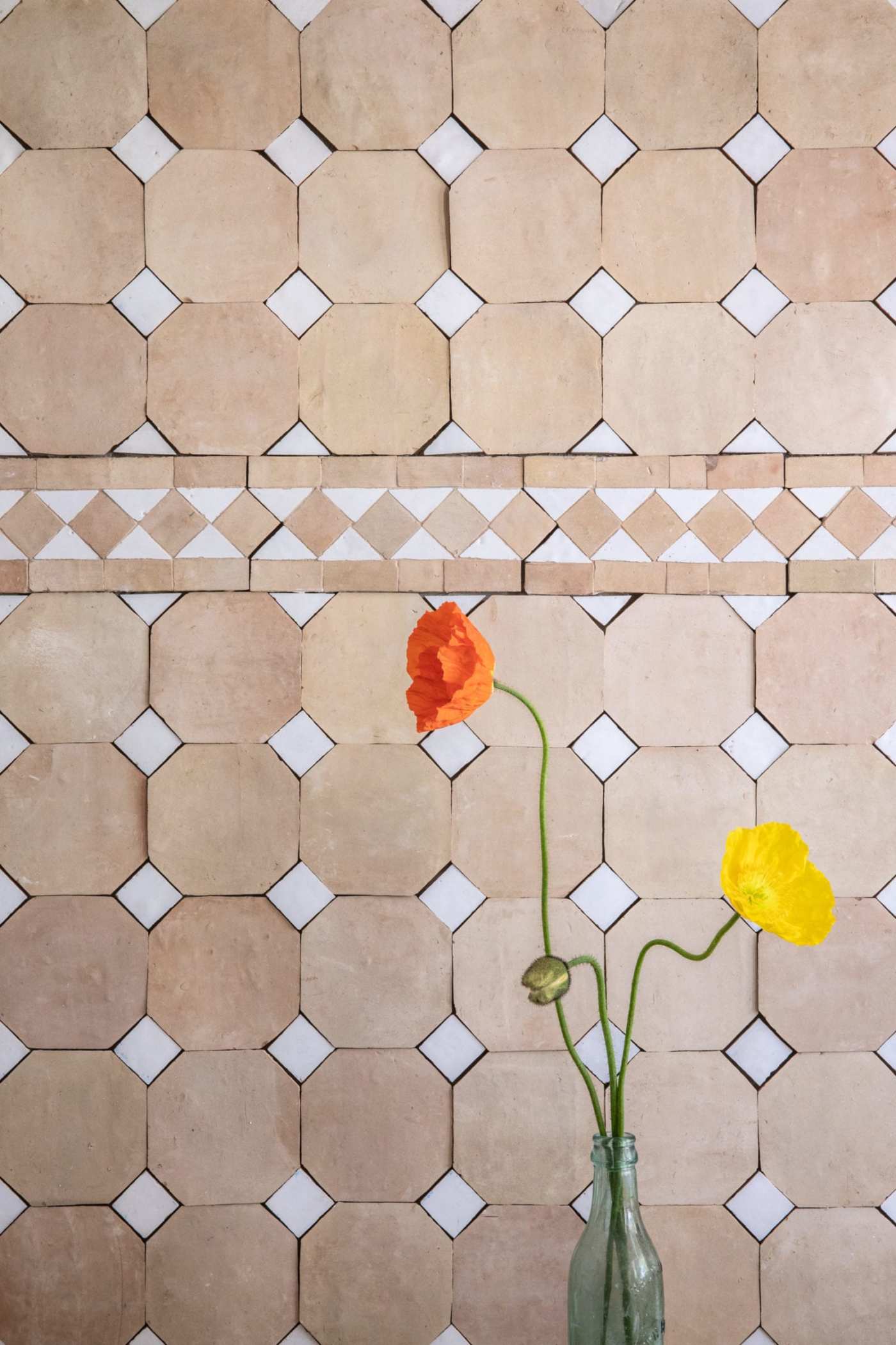 a vase with flowers in front of a tiled wall.