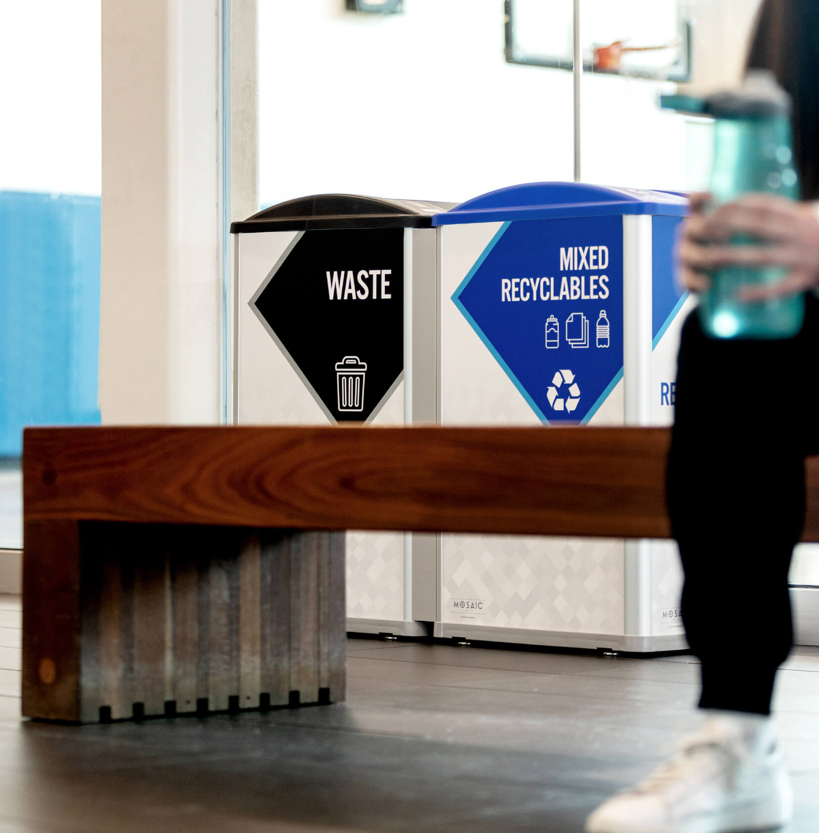 waste and recycling bins inside a fitness center with someone sitting in front on a bench
