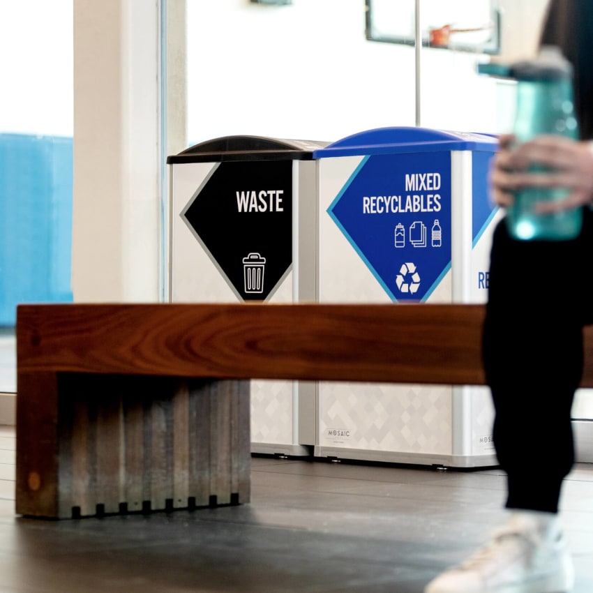 waste and recycling bins inside a fitness center with someone sitting in front on a bench