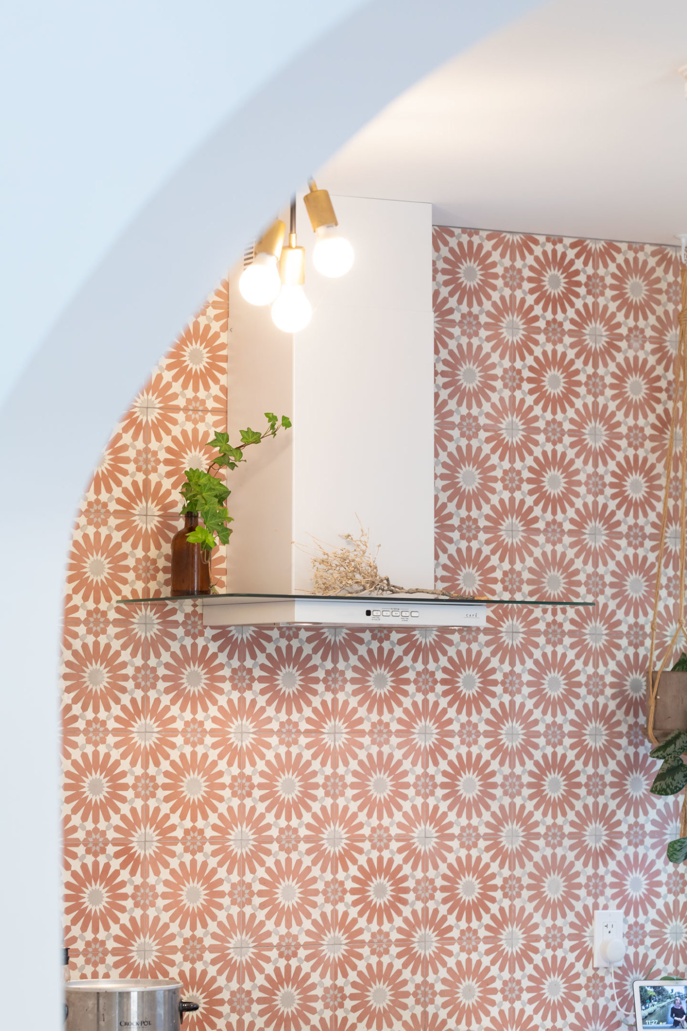 a kitchen with a red and white tiled wall and a shelf with a potted plant.