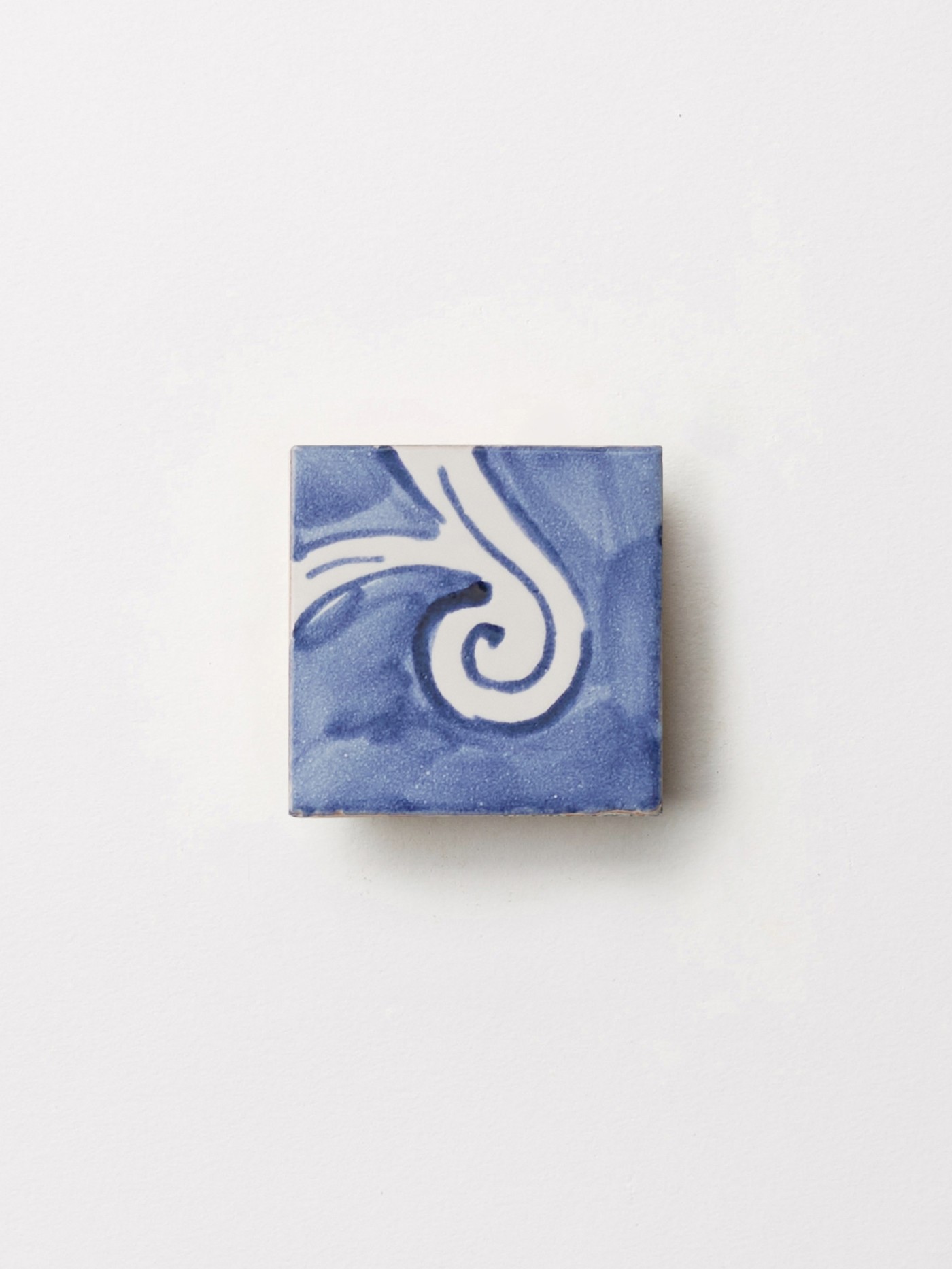 a blue and white tile with a swirl design on top of a white surface.