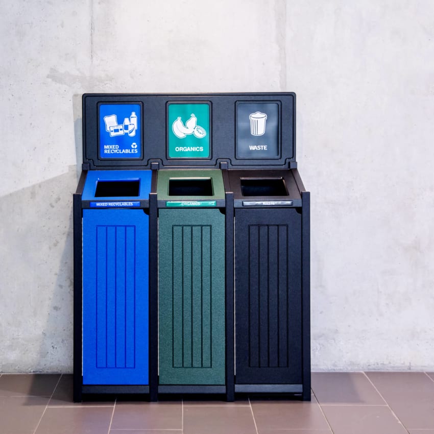 mixed recyclables and waste container in black blue and green against concrete wall in a modern office building