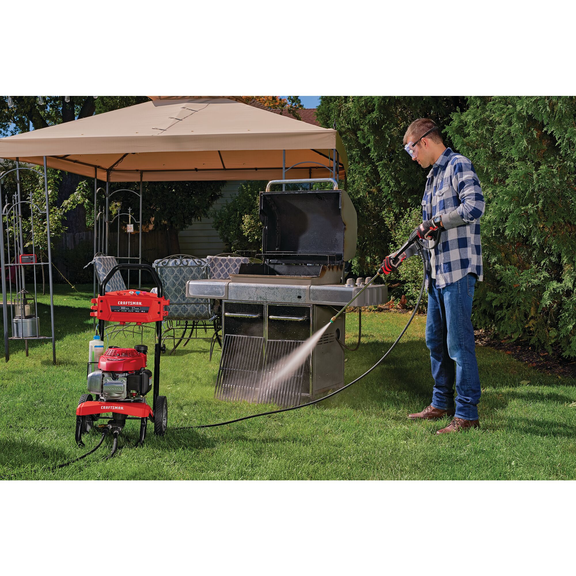 3100 MAX Pounds per Square Inch or 2 and seven tenths MAX Gallons Per Minute Pressure Washer being used by person to wash Bar B Que grills placed outdoors in lawn.