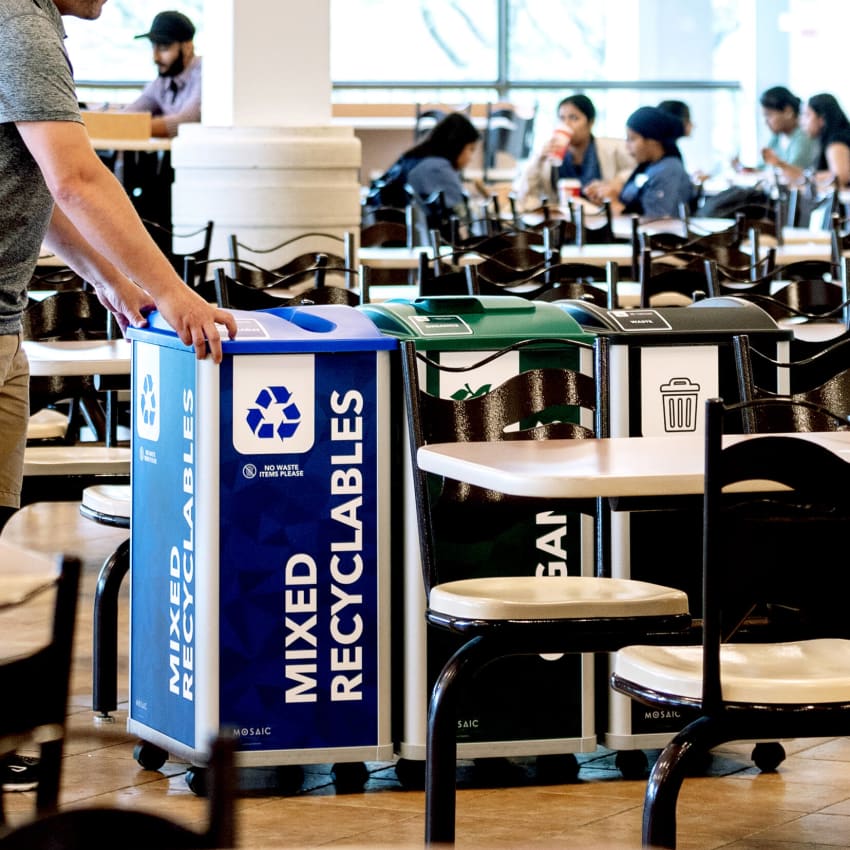 a triple recycling and waste collection station being moved for servicing inside a college cafeteria