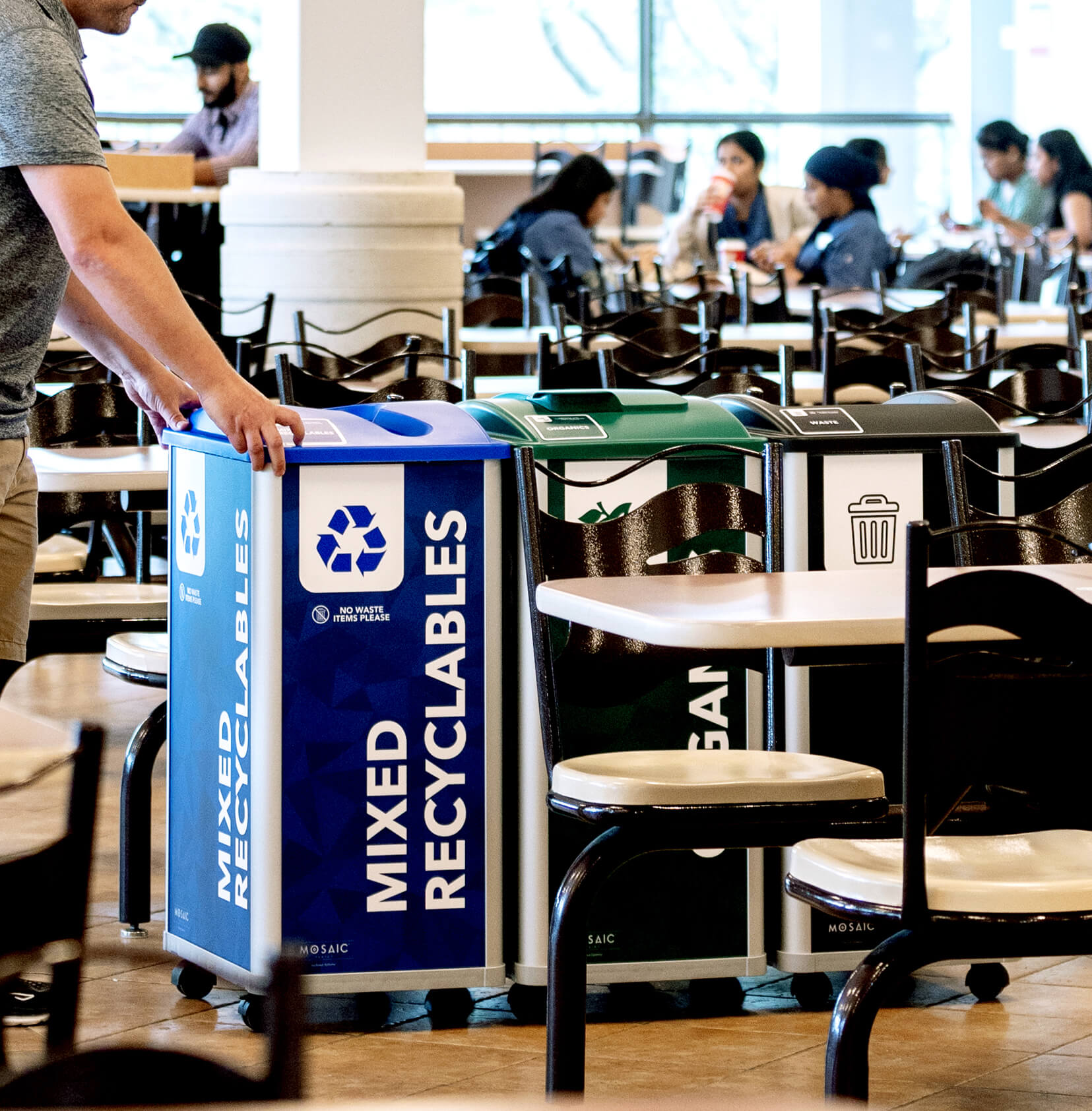 a triple recycling and waste collection station being moved for servicing inside a college cafeteria