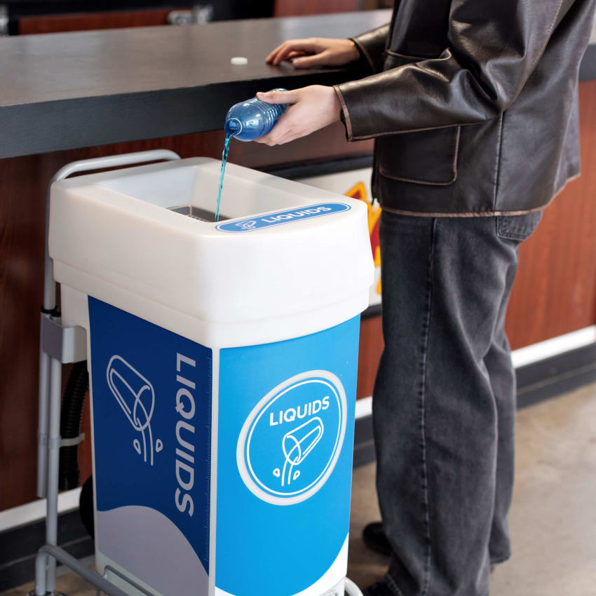 woman pouring liquid into plastic liquid waste collection bin at a restaurant