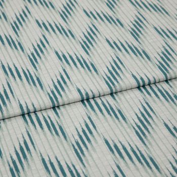 Folded woven fabric with teal ikat-like diagonal stripes and subtle vertical ribbing — folded once, lying flat on a neutral surface, close-up, soft even lighting.