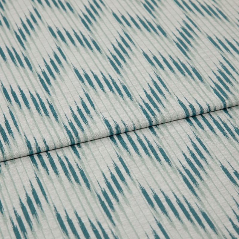 Folded woven fabric with teal ikat-like diagonal stripes and subtle vertical ribbing â€” folded once, lying flat on a neutral surface, close-up, soft even lighting.